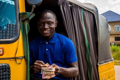 young african man driving a rickshaw taxi counting his money smiling